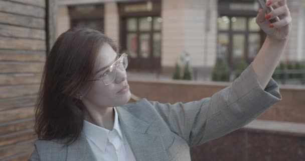 Portret van de mooie aantrekkelijke zakenvrouw in een bril lachend en selfies nemend op de mobiele telefoon buiten. 4k. — Stockvideo