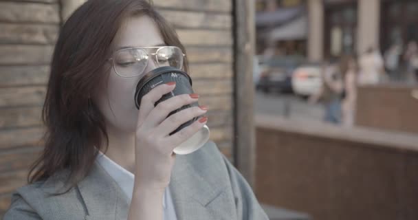Gözlüklü ve takım elbiseli esmer ciddi bir iş kadını birini beklerken kahve içiyor. 4k. — Stok video