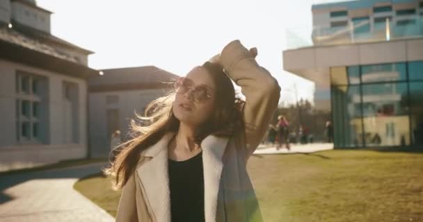 Vita studentesca. Elegante studentessa cammina lungo il passo prima dell'università e scuote i capelli. Donna elegante in abiti casual e occhiali da sole moderni. — Video Stock