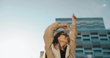 Sonbahar titreşimleri. Genç ve güzel bir kız öğrenci akşam güneşinin altında modern cam binanın önünde saçlarını sallıyor.