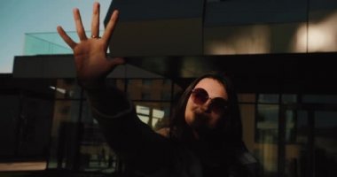 Gün batımı destansı, bayan öğrenci. Yuvarlak kahverengi gözlüklü güzel kız modern cam bina önünde otururken elini güneşe doğru tutar.