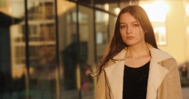 Güzel bir kadın ciddi ciddi kameraya bakar ve akşam güneşinin altın ışıklarında gülümser.