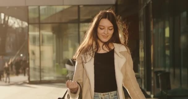 Skákající studentka vypadá šťastně, když kráčí po cestě s taškou v paprscích večerního slunce — Stock video