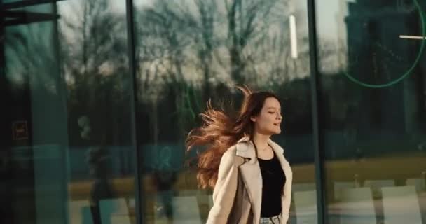 Springen vrouwelijke student ziet er gelukkig wandelen langs de weg met haar tas in de stralen van de avondzon — Stockvideo