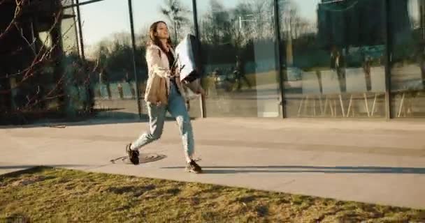 Skoki uczennica wygląda szczęśliwy spacer wzdłuż drogi z torbą w promieniach wieczornego słońca — Wideo stockowe