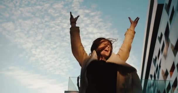 Посмотрите снизу на счастливую и прыгающую девушку, стоящую перед современным стеклянным зданием — стоковое видео