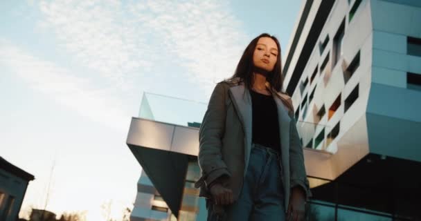 Spójrz od dołu na pewną siebie i poważną młodą kobietę stojącą przed nowoczesnym szklanym budynkiem — Wideo stockowe