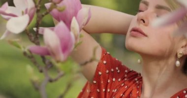 Doğanın tadını çıkaran ve bahar manolyasının çiçeklerine dokunan güzel bir kadın, çiçek açan manolya ağaçlarıyla mutlu, güzel bir kız. Model kokulu çiçek, yavaş çekim.