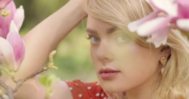 Kadın portresi. Doğal sarı saçlı ve mavi gözlü eğlenceli bir kız. Arka planda çiçek açan pembe bir manolya bahçesi. Bahçenin bahar tazeliği.