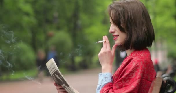 Mooie vrouw die kranten leest en sigaretten rookt in het park. 4K-video. — Stockvideo