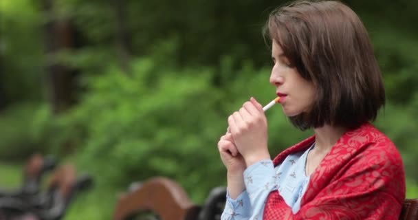 Beautiful woman smokes cigarette in park. 4K video. — Stockvideo