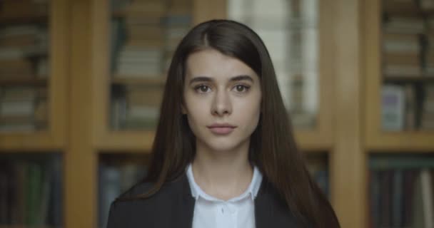 Vrouwelijke student, bibliotheek. meisje kijkt recht in de camera en glimlacht het zetten van haar bril — Stockvideo