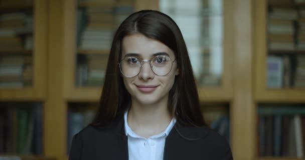 Kvinnlig student, bibliotek. Flickan tittar rakt in i kameran och ler. — Stockvideo