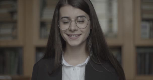 Estudante, biblioteca. Menina olha direto na câmera e sorri. — Vídeo de Stock