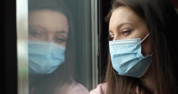 Gros plan femme triste en masque chirurgical visage maigre tête sur vitre regarde à l'extérieur se sent stressé en raison de coronavirus pandémie épidémie mondiale. quarantaine et auto-isolement, rester à la maison arrêt concept covid — Video