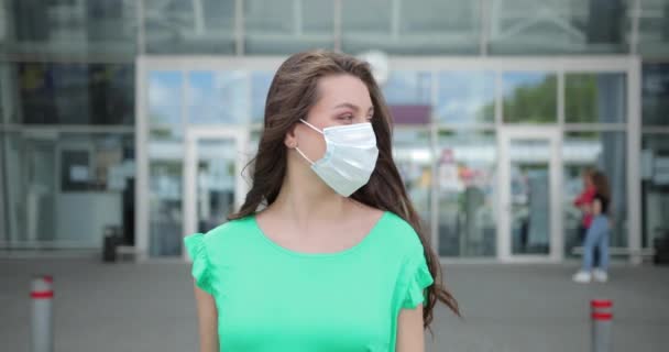 Jovem viajante turista deixa terminal da estação de trem do aeroporto com uma mala de mão e uma máscara de proteção médica. menina estudante hipster elegante andando com saco fundo urbano edifício moderno — Vídeo de Stock