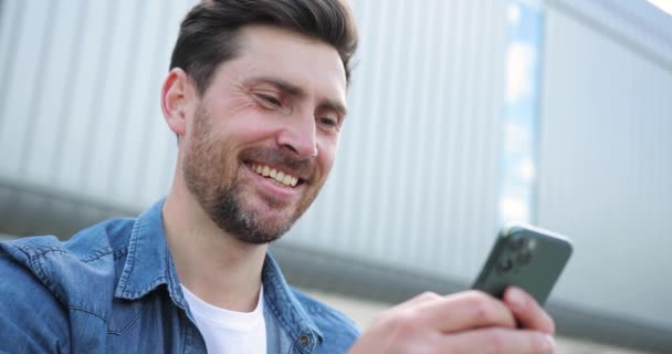 Fiatal, vonzó szakállas férfi sms-ezik egy szmattelefonon. A férfi okostelefont használ és mosolyog.. — Stock videók