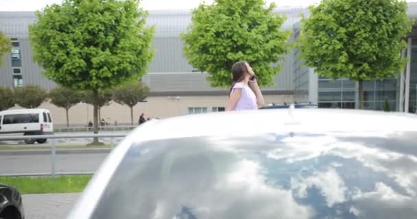 Young pregnant woman traveling on vacation. View of a traveler with a suitcase. A woman with a wheeled travel bag walks near the car park and talk on the phone. — Stock Video