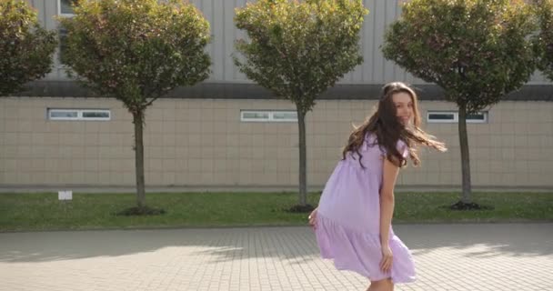 とても陽気で幸せな妊娠中の女性は、紫の妊婦のドレスで通りを歩いて幸せを感じています — ストック動画