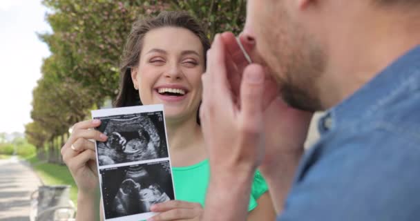 Ευτυχισμένο ζευγάρι που περιμένει τη γέννηση ενός μωρού. Μια γυναίκα δείχνει μια φωτογραφία ενός υπέρηχου στον άντρα της. Συναίσθημα χαράς και ευτυχίας — Αρχείο Βίντεο