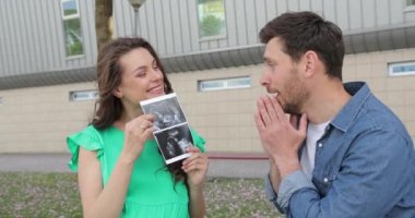 Genç hamile çift gösterisi ve karnında ultrason fotoğrafı olan bir bebek. Annem ve babam mutlu gülümsüyorlar.