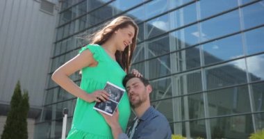 Genç hamile çift. Adam çocuğuyla konuşurken karısının karnını öpüyor. Anne ve baba mutlu gülümserken bebeğe bakıyorlar. Yavaş çekim