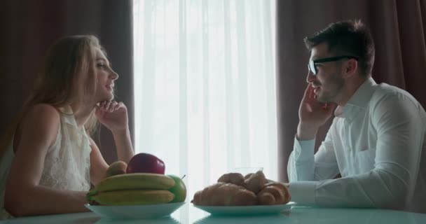 Jeune couple assis à la table et parlant. Sur la table sont des fruits et des croissants. — Video