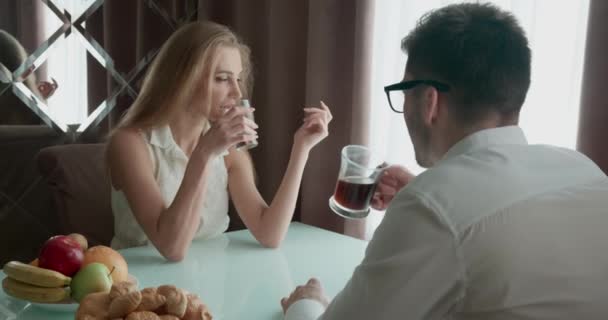 Pareja desayunando en la mesa cerca de la ventana. Hombre beber tee o café. La mujer se emborracha un poco. Jóvenes hablando durante el desayuno. — Vídeos de Stock