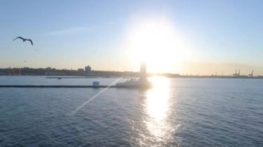 Martı İHA 'nın arkasında uçuyor. Şehir deniz feneri ve iskelesinin arka planında. Güzel gün batımı