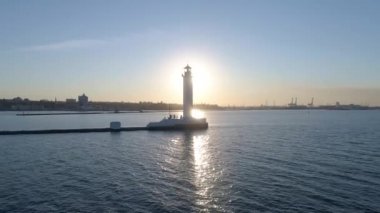 Denizde bir deniz feneri var. Arkasında güneş vardı. Güneş ışınları suyun üzerinde parlıyor. Video bir İHA 'da çekildi. Gün batımı. Gün doğumu