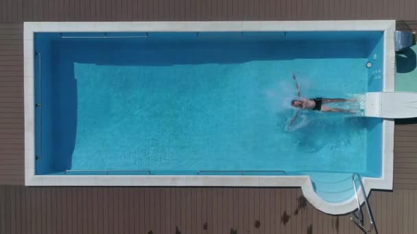 Молодой человек на летних каникулах прыгает головой вперед в чистую голубую воду бассейна для освежения в жаркий солнечный день. Он падает спиной на воду в бассейне. — стоковое видео