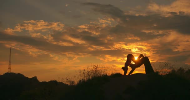 Silueta de mujer joven y hombre haciendo yoga de pareja al atardecer. Meditación. Pareja practicando acro yoga. Ejercicio de flexibilidad en el entorno natural. — Vídeos de Stock