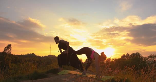 Een paar acro yoga oefeningen buiten. Acro yoga concept. Combineer yoga. Yoga flexibiliteit klasse workout. Mooi stel dat acroyoga doet. Paar die acroyoga beoefenen bij zonsondergang. — Stockvideo