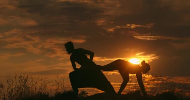 Unga idrottspar gör akroyogaövningar. Silhuett ungt par utövar yoga vid solnedgången. En smal kvinna som gör acro yoga. Vackert par som gör acro yoga. — Stockvideo