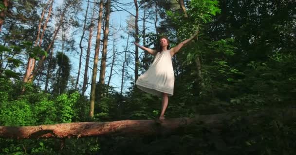 Mujer joven que se relaja al aire libre en el bosque, ella hace la posición del árbol. mujer balansed en una pierna en un árbol caído. En armonía con la naturaleza. — Vídeos de Stock