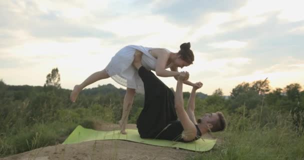 Fit sportief paar oefenen acro yoga met partner samen buiten, het uitvoeren van voorste plank vogel pose, jongeman met vliegende vrouwen armen balanceren op zijn voeten, acrobatische oefening op de — Stockvideo