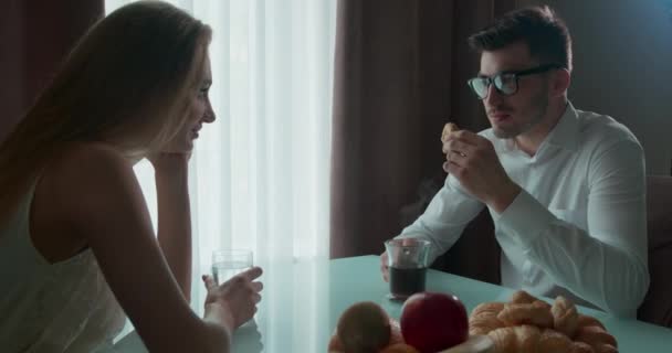 Couple ayant le petit déjeuner à la table près de la fenêtre. Un homme qui mange du croissant. Les jeunes parlent — Video