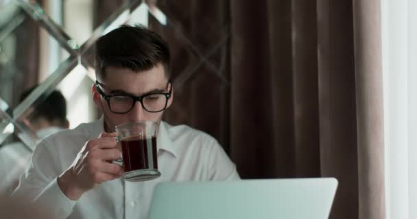 Hombre en vasos sentado a la mesa, trabajando y bebiendo café o te — Vídeos de Stock