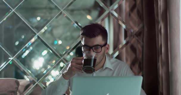 Homem de óculos sentado à mesa, trabalhando e bebendo chá ou café. — Vídeo de Stock