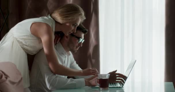 In de kamer bij het raam werken man en vrouw aan een laptop. — Stockvideo