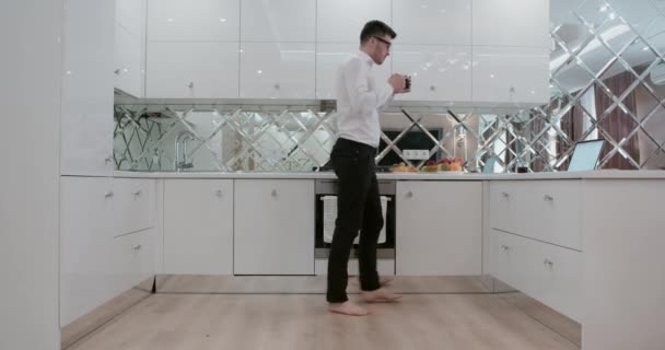 Jeune homme boire un thé ou un café, écouter de la musique et danser à la maison sur une cuisine — Video