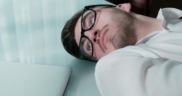 Primer plano video de un hombre en gafas acostado en una mesa mirando triste — Vídeos de Stock