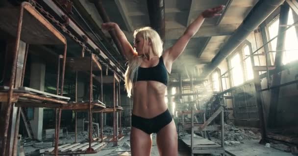 Mulher bonita fitness loira em sportswear realizando exercício de levantamento de braço em uma fábrica — Vídeo de Stock