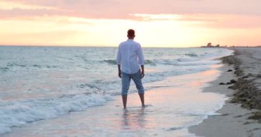 Sahilde duran bir adam okyanusun üzerinde güzel bir gün batımını seyrediyor.