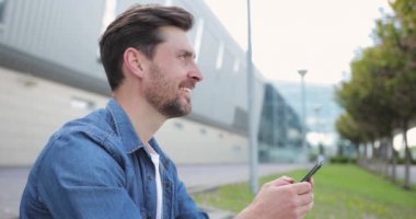 Sokakta gülümseyen ve akıllı telefonuna mesaj yazan çekici bir adam. Genç sakallı adam akıllı telefon kullanıyor. Metin mesajları, sosyal ağlar.