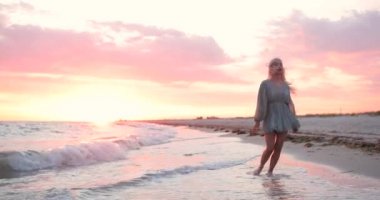 Gün batımında sahilde yürüyen kısa elbiseli güzel sarışın kadın. Stesdicam 'ın çekimini kapat