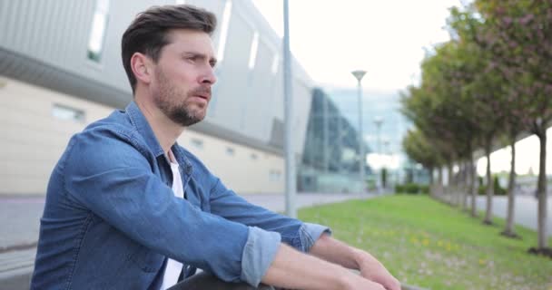 Un hombre atractivo sentado triste en la calle. Joven barbudo en depresión — Vídeos de Stock