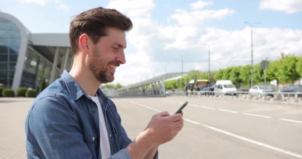 Sokakta gülümseyen ve akıllı telefonuna mesaj yazan çekici bir adam. Genç sakallı adam akıllı telefon kullanıyor. Metin mesajları, sosyal ağlar — Stok video