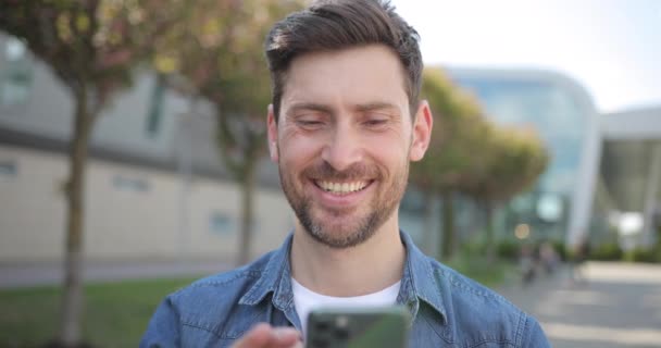 Успішна щаслива людина пише СМС-повідомлення на своєму сучасному Смартфоні. Молода людина йде, маючи хороший Mood, дивлячись Задоволений. Успішне життя. — стокове відео