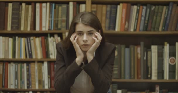 Γυναίκα φοιτήτρια, βιβλιοθήκη. Θλιβερό κορίτσι στέκεται μπροστά από τα ράφια των βιβλίων στη βιβλιοθήκη — Αρχείο Βίντεο